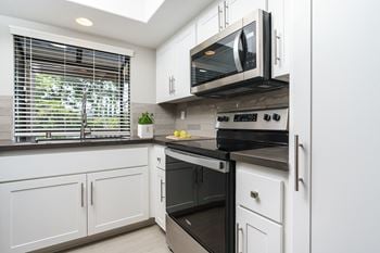 A kitchen with white cabinets and black appliances and a window